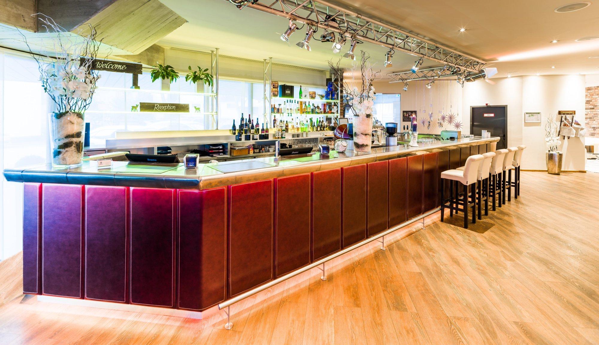Hell beleuchtete Hotelbar mit Barhockern und einem großen Getränkesortiment
