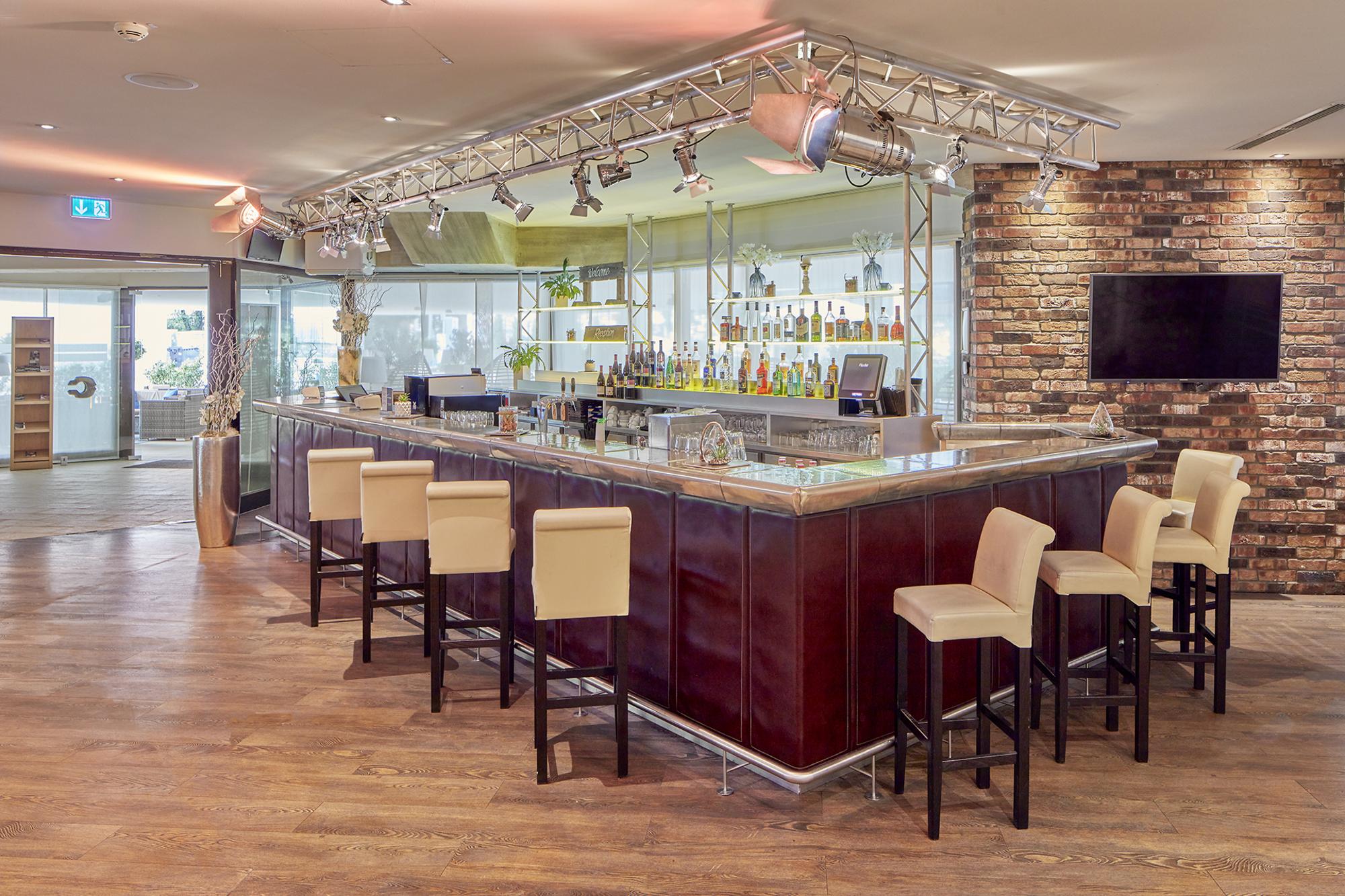 Hell beleuchtete Hotelbar mit Barhockern und einem großen Getränkesortiment