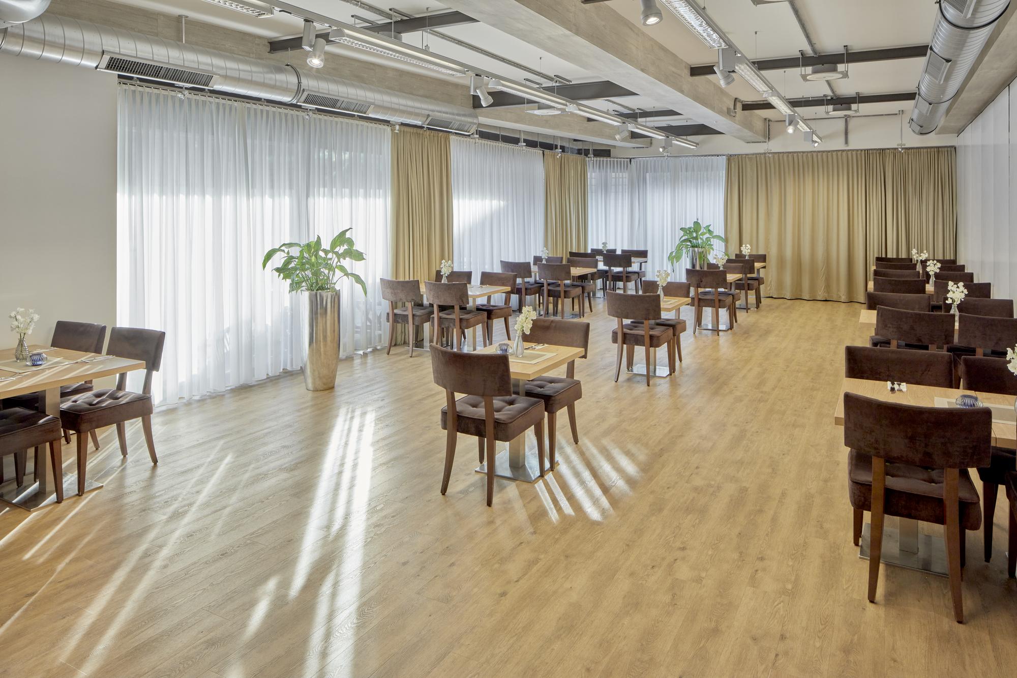 Heller Frühstücksraum mit großer Fensterfront und diversen Tischgruppen unterschiedlicher Größe