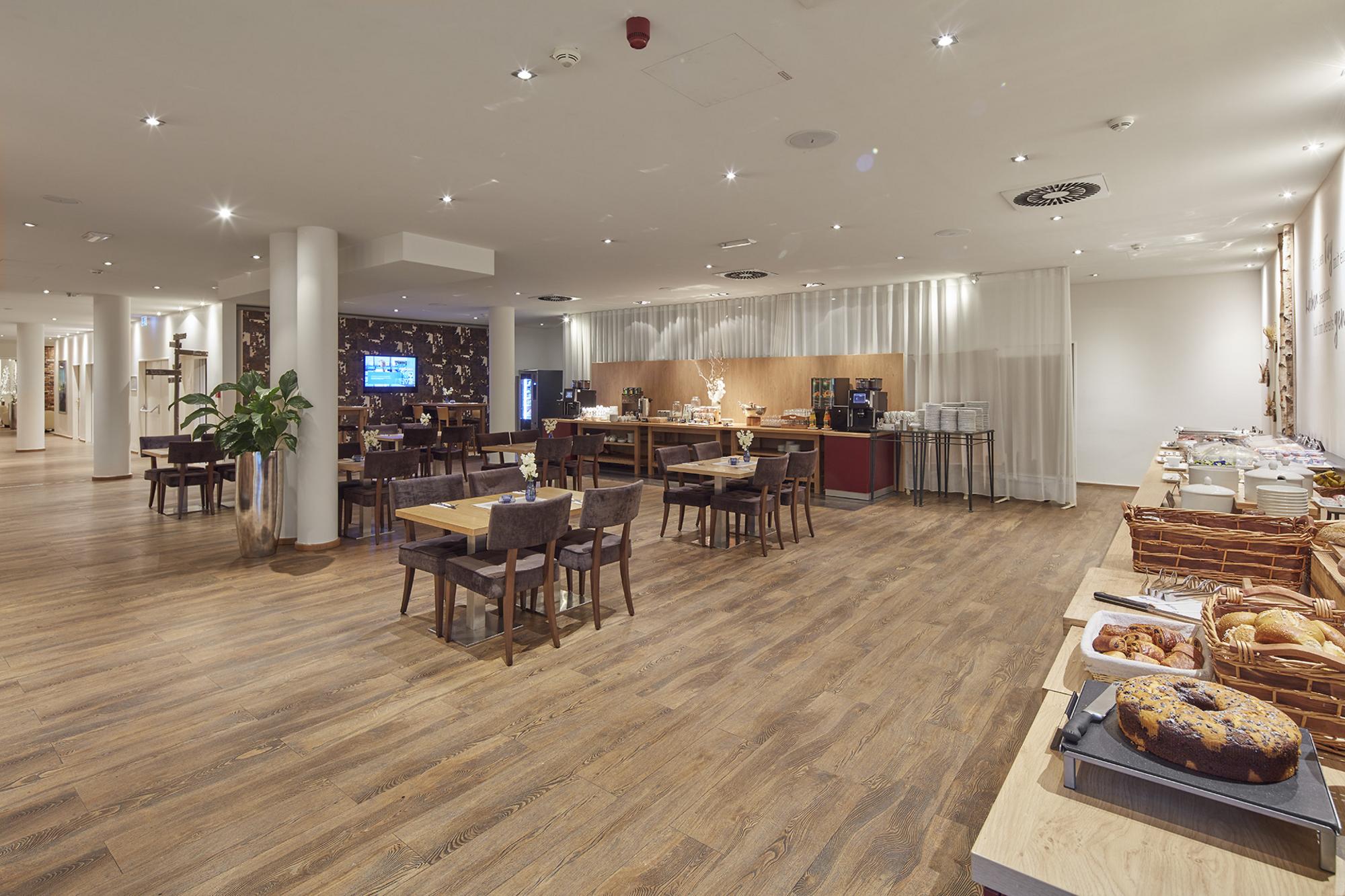 Heller Frühstücksraum mit großem Frühstücksbuffet und diversen Tischgruppen unterschiedlicher Größe