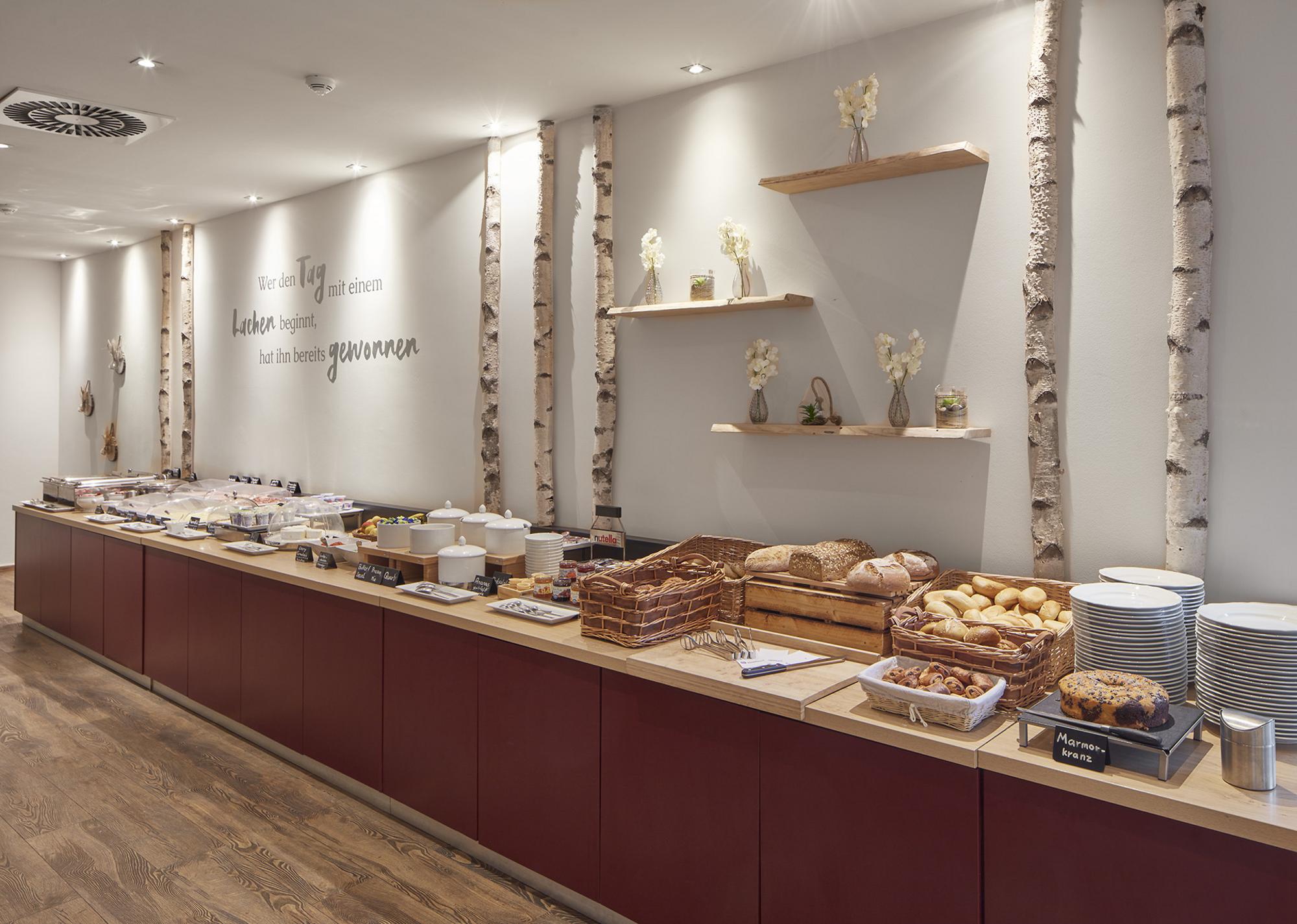 Heller Frühstücksraum mit großem Frühstücksbuffet und Birkenholz-Elementen an der Wand